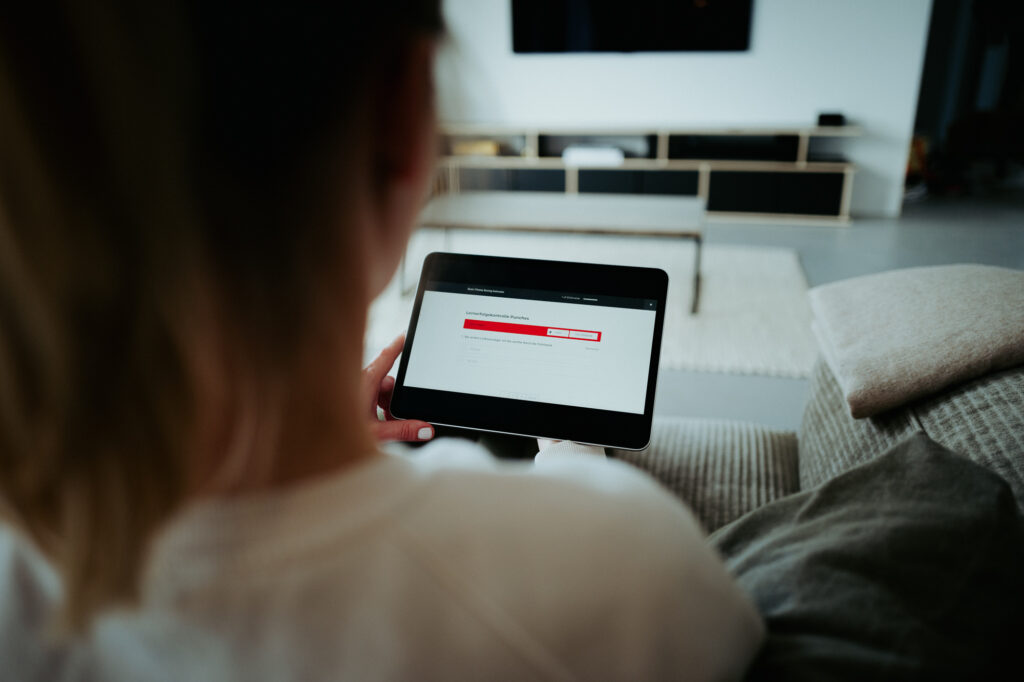 Boxtrainer per Fernlehrgang. Teilnehmer sitzt zu Hause auf dem Sofa mit Tablet und loggt sich in den Online-Kurs ein.